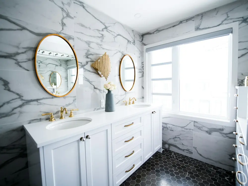 Bathroom with book-matched white and grey veined marble walls, brass fittings and a double vanity