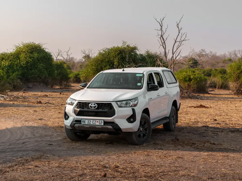 A white Toyota Hilux dual cab parked on a red dirt clearing