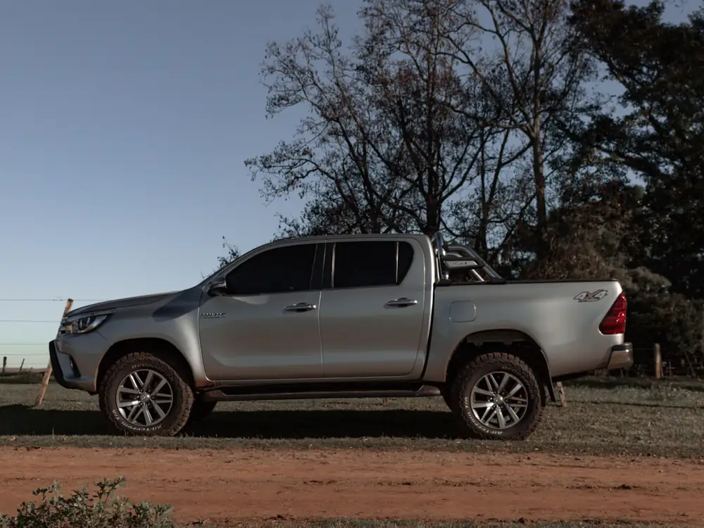 Silver Hilux dual cab ute parked on a dirt road beside a fence