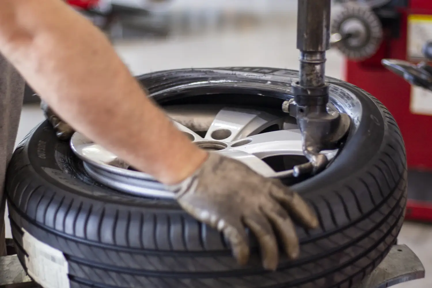 A tyre fitter's gloved hands fitting a new tyre onto an alloy wheel on the tyre machine