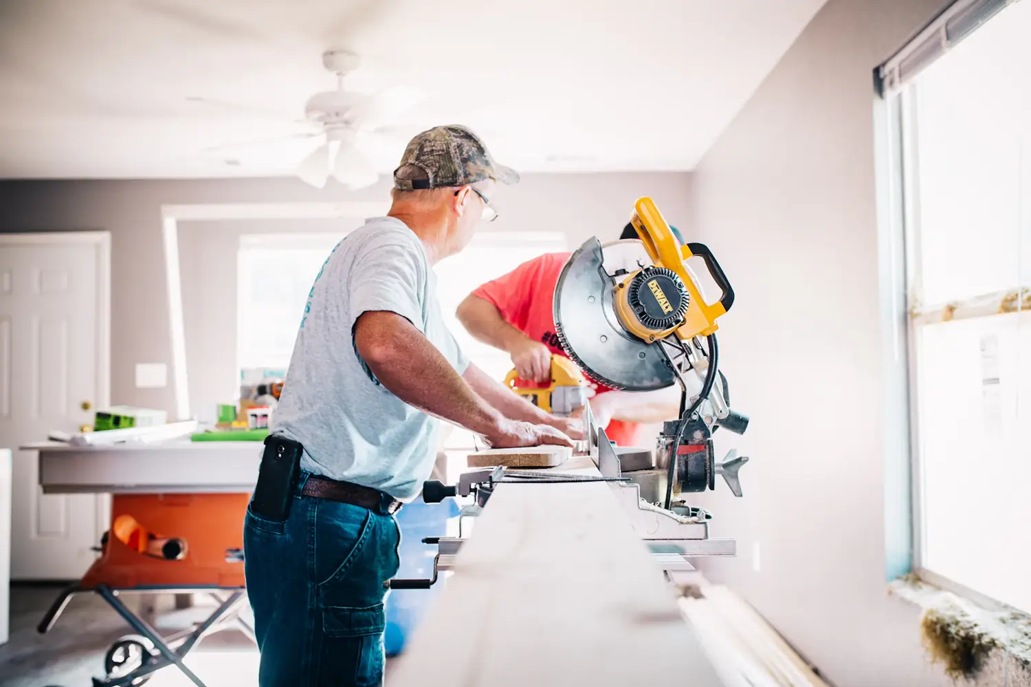 Two carpenters cutting timber on a mitre saw inside a house being renovated